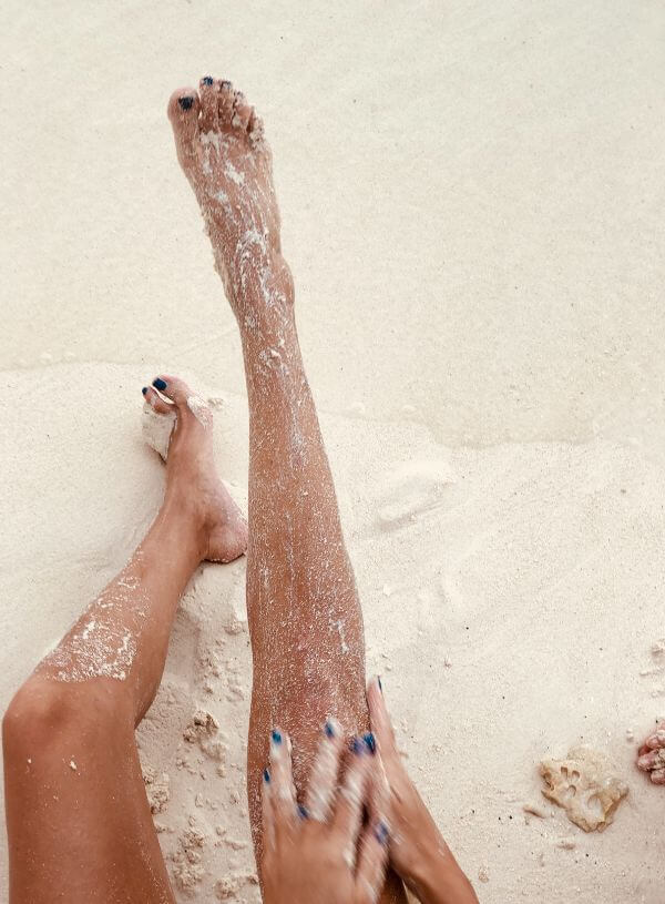 A lady scrubbing her leg with sand on the beach